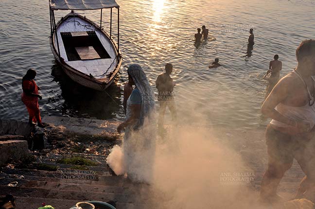 Travel- Varanasi the city of light (India) - Devotees taking bath and women burning some waste material at the bank of Holy River Ganges at Varanasi, Uttar Pradesh, India. by Anil