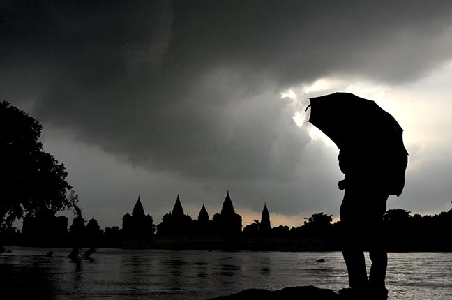 Monuments- Palaces and Temples of Orchha - Orchha, Madhya Pradesh, India- August 20, 2012: Chhatris on the bank of river Betwa, a tourist holding umbrella enjoying cloudy- rainy weather at Orchha, Madhya Pradesh, India. by Anil