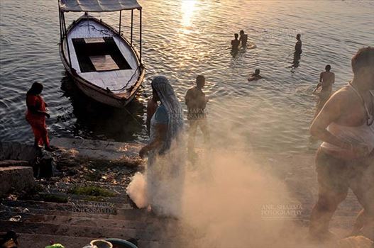 Devotees taking bath and women burning some waste material at the bank of Holy River Ganges at Varanasi, Uttar Pradesh, India.