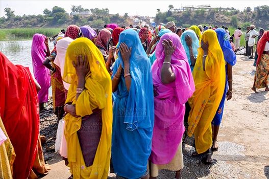 Baneshwar, Dungarpur, Rajasthan, India- February 14, 2011: Bhil women in brightly coloured veils and saris covering their faces ready for the ritual bath at Baneshwar, Dungarpur, Rajasthan, India.